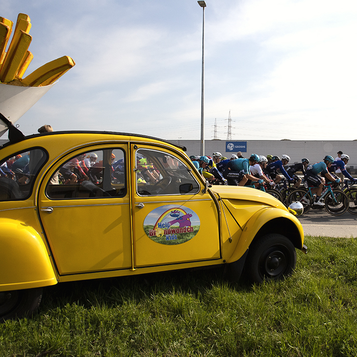 Scheldeprijs 2023 - The peloton passes a Citroen 2CV with a large model of a portion of frites fastened to its back